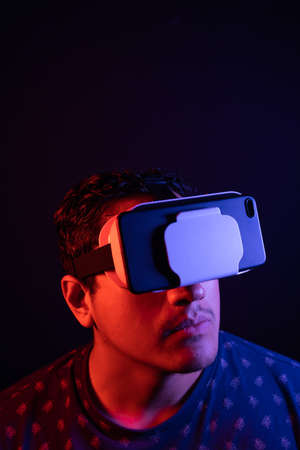 Young latin man using Virtual Reality VR Headset 3D Glasses. Studio dark backdrop. Low key. Copy...