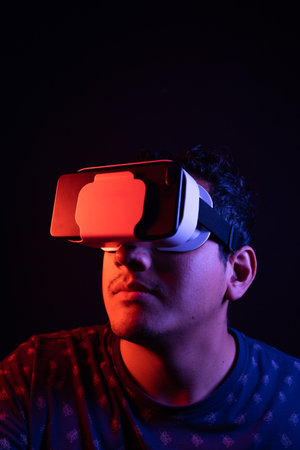 Young latin man using Virtual Reality VR Headset 3D Glasses. Dark backdrop. Low key. Copy space.