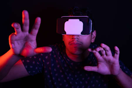 Young latin man using Virtual Reality VR Headset 3D Glasses, extends his hands to hold something....