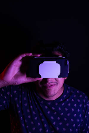 Young latin man using Virtual Reality VR Headset 3D Glasses. Dark backdrop. Low key. Copy space