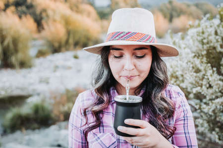 Young caucasian woman with a hat, drinking mate in a natural space with a summer vibe.