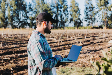 Young latin farmer man teleworking on his laptop in the middle of his plantation . Agricultural sustainability. Wirelessの写真素材