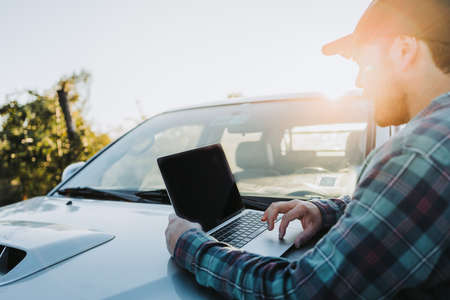 Young latin farmer man on his pickup truck and working on his laptop. Agricultural concept.の写真素材