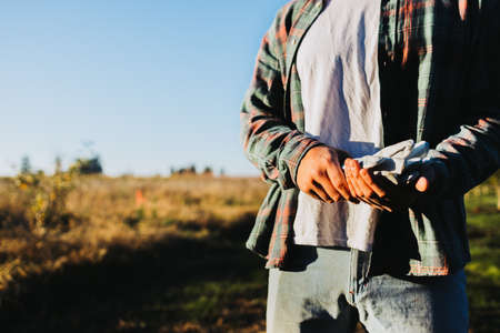 Unrecognizable farmer man holding gardening gloves in the middle of the field. Agricultural sustainability concept.の写真素材