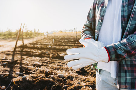 Unrecognizable farmer man wearing gardening gloves in the middle of the farmland. Agricultural...