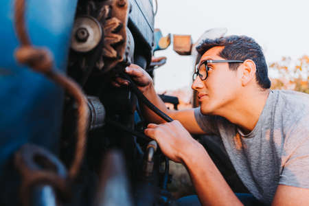 Latin farmer man repairing mechanical problems of an old blue tractor.の写真素材