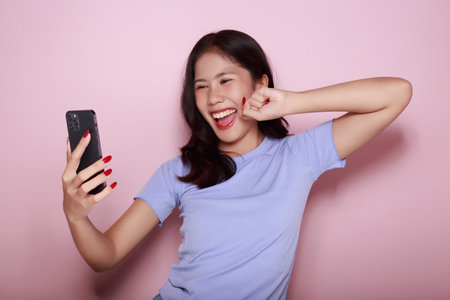 Asian woman cheerfully posing with a mobile, A beautiful young woman is feeling cheerful and happy., half body photo of nice positive lady, Portrait of a beautiful young woman in a light pink background,の写真素材