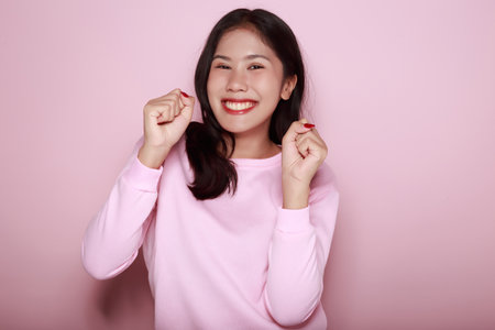 Asian woman doing cheerful pose, Portrait of a friendly young woman smiling happily, Portrait of a beautiful young woman in a light pink background,の写真素材