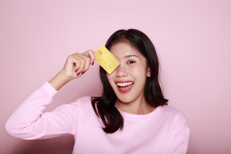 Asian woman holding a credit card in her hand Holding a debit card in hand A beautiful young woman was feeling very happy and excited. Portrait on a light pink backgroundの写真素材