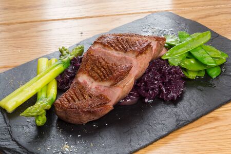 Fried beef tongue with beetroot and pea pods, asparagus on wooden board.の写真素材