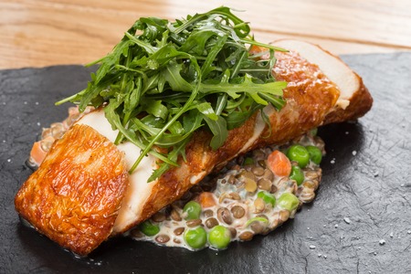 Fried chicken roll with lentils, fresh peas, carrots and gravy, garnished arugula on a black stone...