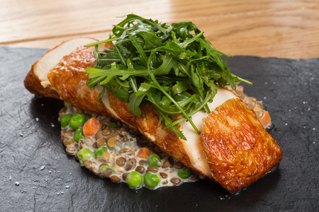 Fried chicken roll with lentils, fresh peas, carrots and gravy, garnished arugula on a black stone plate and a wooden countertop.の写真素材