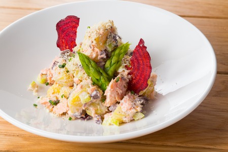 Salad of potatoes, beans, salmon decorated with chips of beets and asparagus on a white plate on a wood.の写真素材