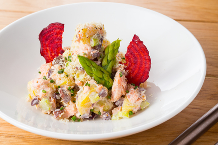 Salad of potatoes, beans, salmon decorated with chips of beets and asparagus on a white plate on a wood.の写真素材
