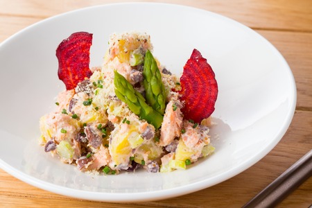 Salad of potatoes, beans, salmon decorated with chips of beets and asparagus on a white plate on a wood.の写真素材