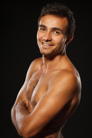 Young muscular smiling male shirtless standing with folded hands over black backgroundの写真素材