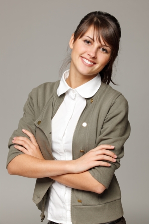 Portrait of young smiling female standing with folded hands, over grey backgroundの写真素材