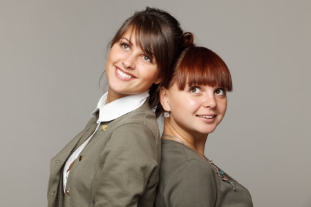 Closeup of two smiling girls standing back to back looking upwards, over grey backgroundの写真素材