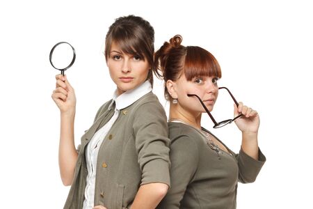 Two serious girls standing with magnifying glass and old fashioned eyeglasses, isolated on white backgroundの写真素材