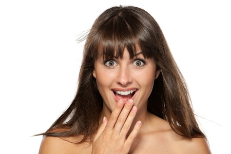 Surprised young woman with hands over her mouth laughing against white backgroundの写真素材