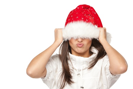 Playful cute young woman in Santa hat having fun pulling down the hat over the eyes on white background の写真素材