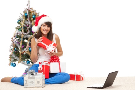 Calm female sitting near Christmas tree on the floor with many gifts and laptop, over white backgroundの写真素材