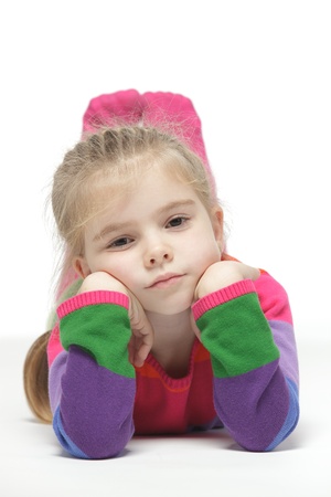 Little pensive girl lying down on the floor, over white backgroundの写真素材