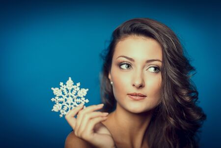 Closeup portrait of beautiful woman with snowflake with copy space looking to the side, over blue backgroundの写真素材