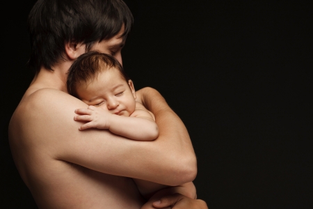 Father holding newborn baby over black backgroundの写真素材