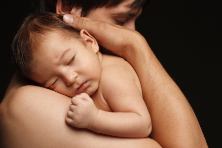 Closeup of sleeping newborn baby in the embraces of his father over black backgroundの写真素材