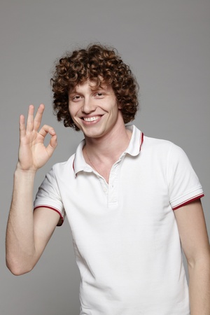 Closeup of smiling young man gesturing okay sign over gray backgroundの写真素材