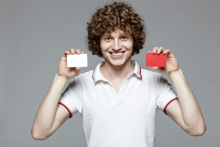 Portrait of the young smiling man holding two blank credit cards, isolated on gray backgroundの写真素材