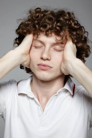 Portrait of young man with headache holding forehead in pain over gray backgroundの写真素材