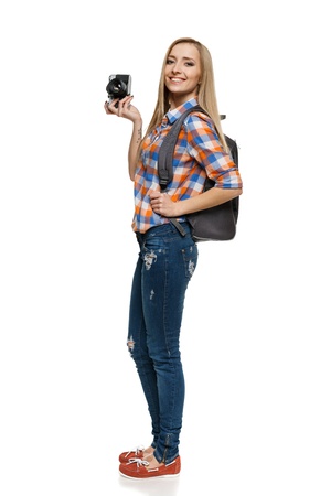Full length of young female with backpack holding camera over white backgroundの写真素材
