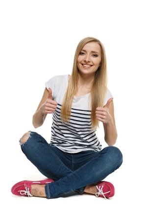 Happy young female sitting on floor showing thumb up signs, isolated on white backgroundの写真素材