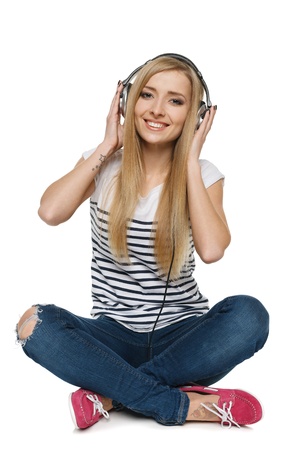 Happy young female sitting on floor enjoying music in headphones, isolated on white backgroundの写真素材