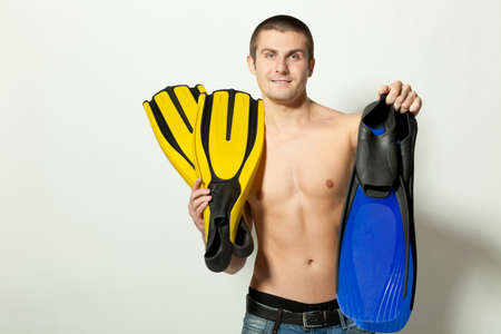Young attractive Caucasian man in jeans topless holding two pairs of flippers の写真素材