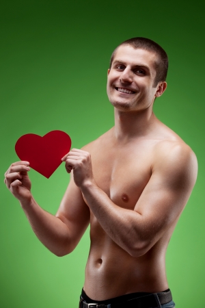 Smiling male model shirtless holding heart shape, over green backgroundの写真素材