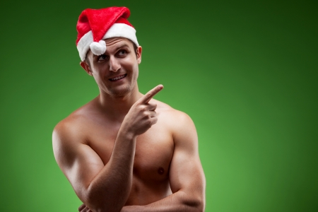 Shirtless muscular man wearing Santa hat pointing upwards, over green backgroundの写真素材