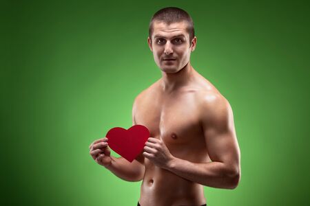 Smiling male model shirtless holding heart shape, over green backgroundの写真素材