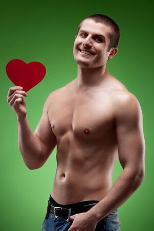 Smiling male model shirtless holding heart shape, over green backgroundの写真素材