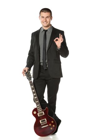 Full length of young man in a suit standing leaning on the guitar showing OK sign over white backgroundの写真素材