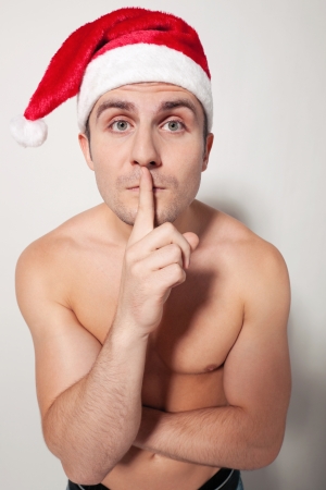 Funny image of young muscular man shirtless wearing Santa  with finger on lips, high angle of viewの写真素材