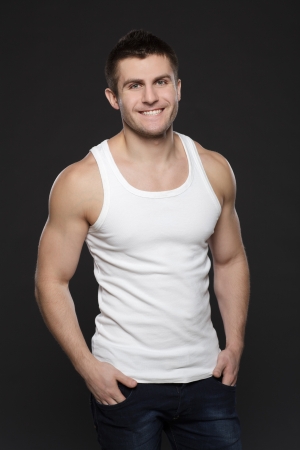 Young handsome muscular man in white t-shirt posing with his hands in pockets over dark backgroundの写真素材