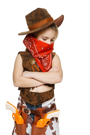 Little pensive girl wearing cowboy costume standing with folded hands looking down, over white backgroundの写真素材