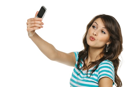 Happy young girl making funny face while taking pictures of herself through cellphone, over white backgroundの写真素材
