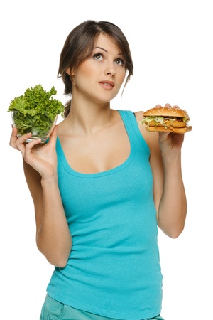 Pensive woman making decision between healthy salad and fast food, over white backgroundの写真素材