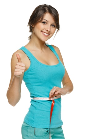 Beautiful woman measuring her waist with a measuring tape and showing thumb up, over white background