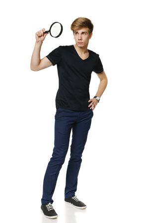 Young trendy man in full length looking trough the magnifying glass, over white backgroundの写真素材