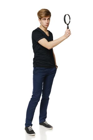 Young trendy man in full length looking trough the magnifying glass, over white backgroundの写真素材